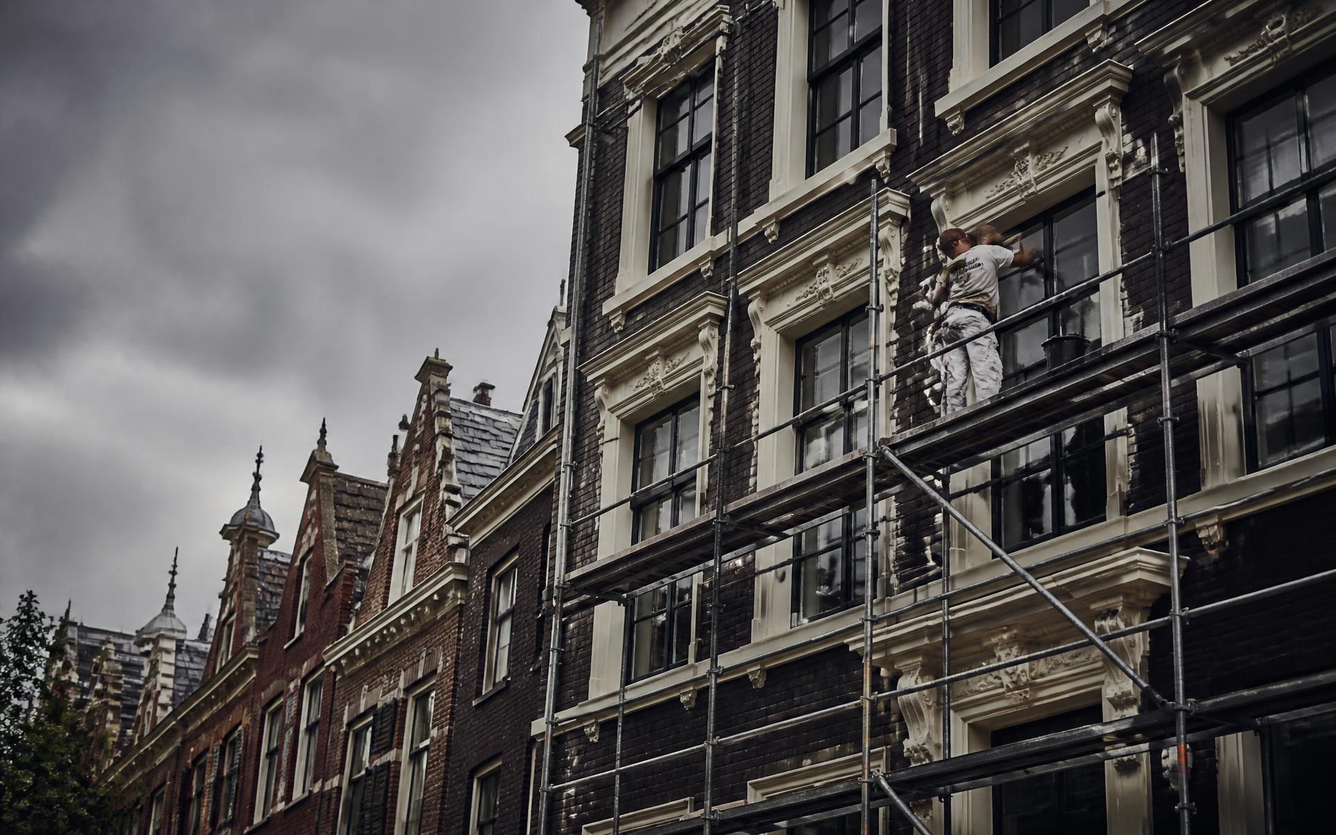 Vakman aan het werk op een steiger langs een Haagse bakstenen gevel